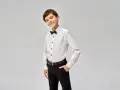 Elegancki chłopiec w białej koszuli z czarną muszką i spodniach. Idealny przykład, jak ubrać chłopca do komunii.