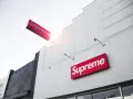 Znak Supreme na białej fasadzie budynku. Supreme to marka znana z limitowanych kolekcji streetwear.