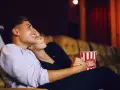 Para randkę do kina wybierz wygodny, ale stylowy strój. Para siedzi blisko siebie, trzymając popcorn.