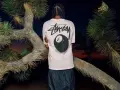 Mężczyzna w koszulce Stussy z grafiką kuli bilardowej 8 i logo Nike. Stussy to kultowa marka streetwearowa.