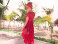 Kobieta w zwiewnej, **czerwonej sukience boho** w białe grochy, z czerwoną opaską na głowie, pozuje na tle palmy i plaży.