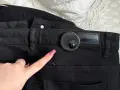 Palec wskazujący z różowym lakierem zbliża się do czarnego klipsa magnetycznego na spodniach. Dowiedz się, jak ściągnąć klips magnetyczny z ubrania.