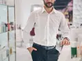 Elegancki mężczyzna w białej koszuli i czarnych spodniach. Pokazuje, jak nosić koszulę, by wyglądać stylowo.
