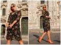 Kobieta w kwiecistej sukience i pomarańczowych szpilkach przed katedrą. Czy buty w kwiaty są modne? Te pomarańczowe zdecydowanie tak!