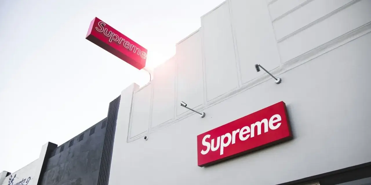 Znak Supreme na białej fasadzie budynku. Supreme to marka znana z limitowanych kolekcji streetwear.