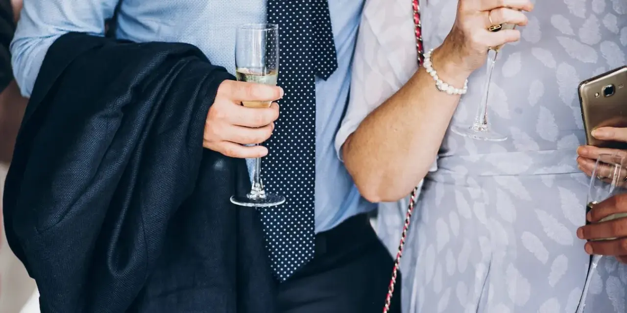 Elegancki mężczyzna w garniturze i krawacie, trzymający kieliszek szampana. To idealny strój, co się ubiera na bierzmowanie.