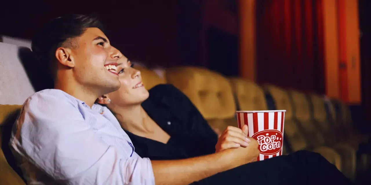 Para randkę do kina wybierz wygodny, ale stylowy strój. Para siedzi blisko siebie, trzymając popcorn.