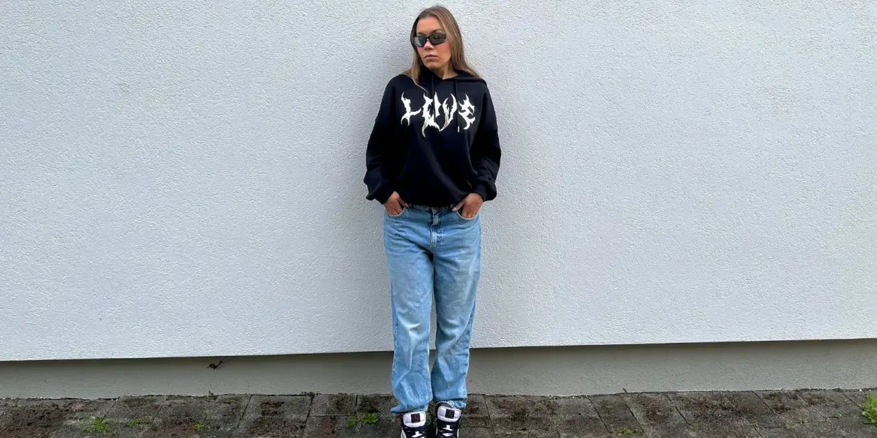 Dziewczyna w czarnej bluzie z kapturem i jeansach, idealny outfit, jak się ubrać na koncert hip hopowy.
