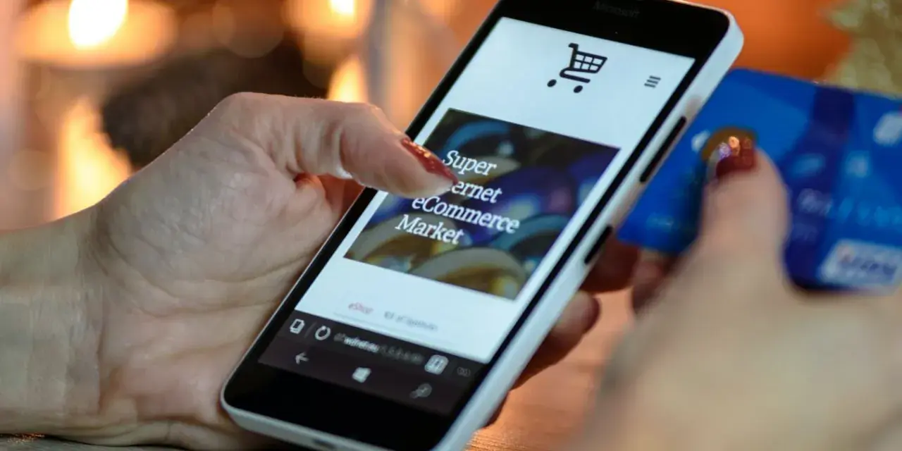 Kobieta z kartą kredytową w dłoni przegląda na smartfonie stronę e-commerce, ucząc się, jak sprzedawać bieliznę w internecie.