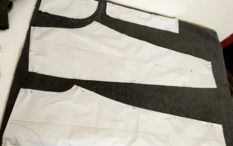 Wykroje papierowe do spodni (przód i tył) przypięte do ciemnego materiału. Rozpoczynamy proces, jak zrobić wykrój spodni.