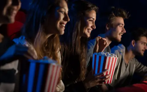 Uśmiechnięci ludzie jedzą popcorn w kinie. Idealny strój do kina to coś wygodnego, jak na przykład bluza.