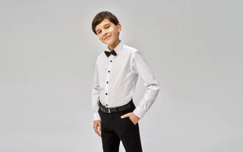 Elegancki chłopiec w białej koszuli z czarną muszką i spodniach. Idealny przykład, jak ubrać chłopca do komunii.