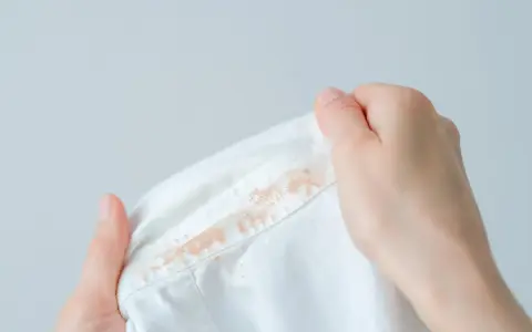 Dłonie trzymają białą koszulę z plamami po fluidzie. Jak sprać fluid? Podpowiedź na zdjęciu.