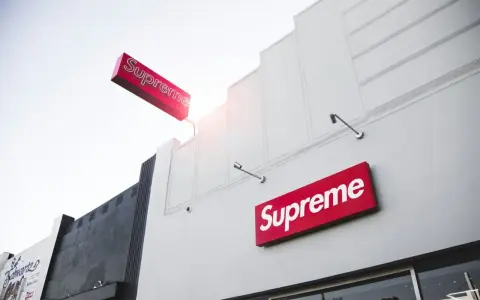 Znak Supreme na białej fasadzie budynku. Supreme to marka znana z limitowanych kolekcji streetwear.