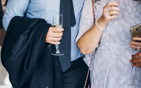 Elegancki mężczyzna w garniturze i krawacie, trzymający kieliszek szampana. To idealny strój, co się ubiera na bierzmowanie.