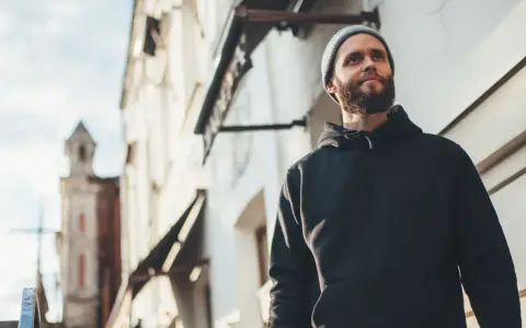 Mężczyzna w czarnej bluzie z kapturem i czapce beanie patrzy w górę. Stylowy sposób, jak nosić bluzę z kapturem.