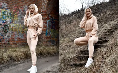 Dresy damskie szerokie w beżowym kolorze, idealne na co dzień. Modelka prezentuje je na tle ceglanej ściany i schodów.