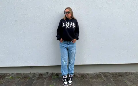 Dziewczyna w czarnej bluzie z kapturem i jeansach, idealny outfit, jak się ubrać na koncert hip hopowy.