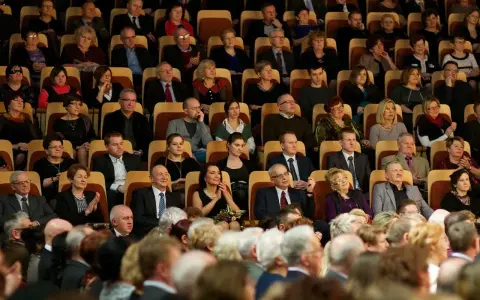Elegancko ubrani ludzie siedzą w filharmonii. Panie w sukienkach, panowie w garniturach. To inspiracja, jak się ubrać do filharmonii.
