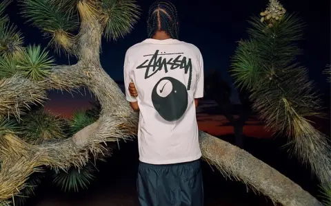 Mężczyzna w koszulce Stussy z grafiką kuli bilardowej 8 i logo Nike. Stussy to kultowa marka streetwearowa.