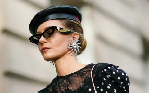 Kobieta w czarnym beretce i okularach przeciwsłonecznych, z dużą, błyszczącą kolczykiem. Czy grochy są modne? Ta stylizacja sugeruje, że tak!