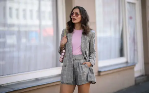 Elegancka stylizacja: co ubrac do spódnico spodenek? Szary garnitur w kratę, różowy top i modna torebka.