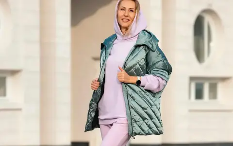 Uśmiechnięta kobieta w pastelowym komplecie dresy z wysokim stanem damskie i błyszczącej kurtce.