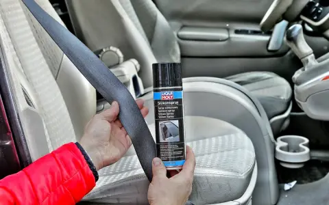 Ręce trzymają pas bezpieczeństwa i puszkę z napisem "Silikonspray". Dowiedz się, jak usunąć silikon z materiału w samochodzie.