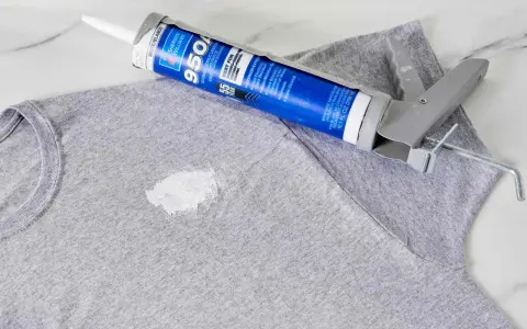 Zaschnięty silikon na szarym T-shircie i pistolet do jego aplikacji. Dowiedz się, jak usunąć zaschnięty silikon z ubrania.
