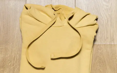Żółta bluza z kapturem złożona na drewnianej podłodze. Dowiedz się, jak złożyć bluzę z kapturem, aby zaoszczędzić miejsce.