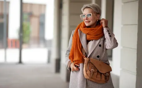 Elegancka kobieta w płaszczu w drobną kratę i pomarańczowym szalu. Czy krata pogrubia? Ten styl pokazuje, że niekoniecznie!