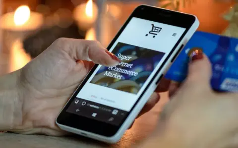 Kobieta z kartą kredytową w dłoni przegląda na smartfonie stronę e-commerce, ucząc się, jak sprzedawać bieliznę w internecie.