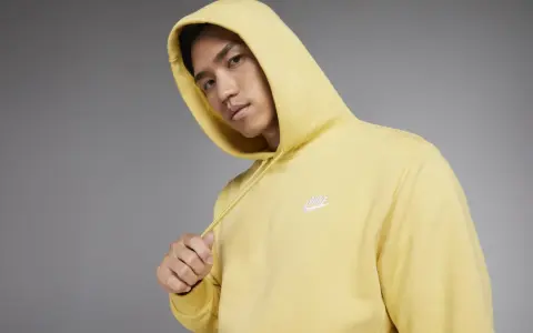 Młody mężczyzna w żółtej bluzie z kapturem Nike Club.