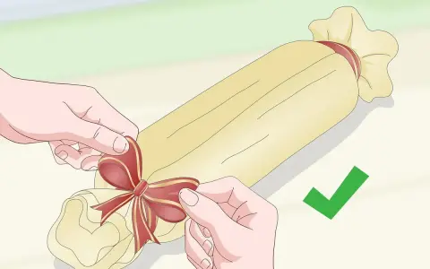Ręce wiążą wstążkę na zapakowanym w papier prezentowym podłużnym przedmiocie.