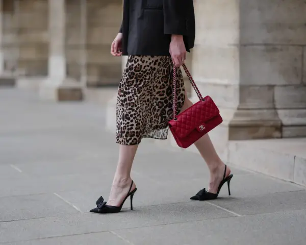 Elegancka kobieta w sukience w panterkę i czarnym blazerze, z czerwoną torebką Chanel. Czy sukienka w panterkę jest modna? Zdecydowanie tak!