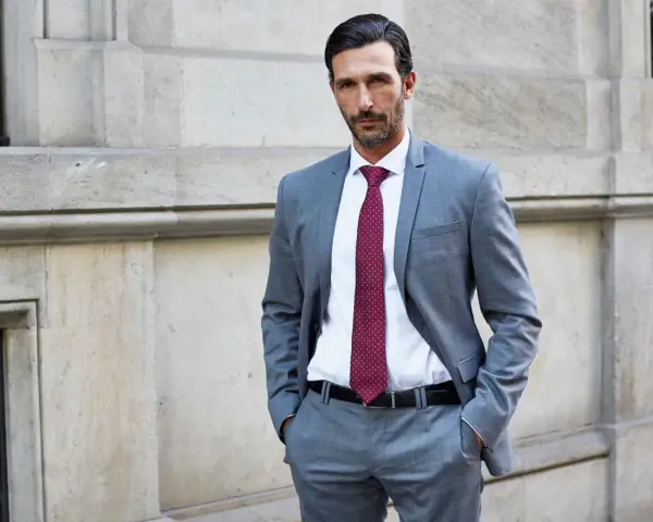 Elegancki mężczyzna w szarym garniturze i bordowym krawacie. Idealna stylizacja, jak ubrać się na komunię mężczyzna, by wyglądać szykownie.