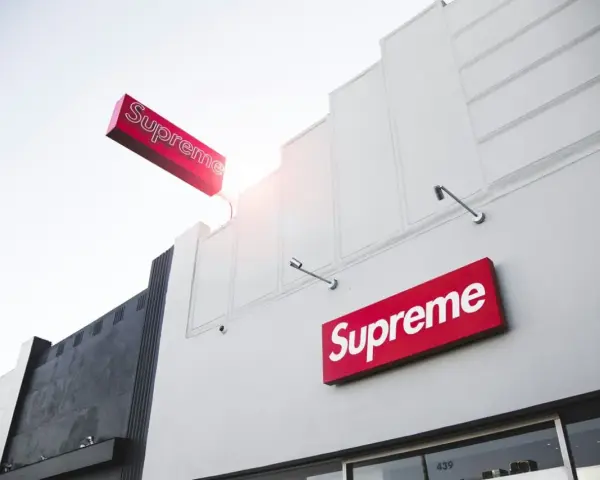 Znak Supreme na białej fasadzie budynku. Supreme to marka znana z limitowanych kolekcji streetwear.