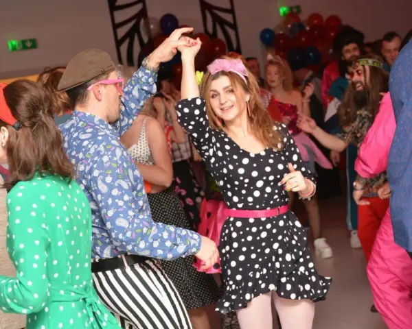 Impreza w stylu PRL! Kobieta w grochy i mężczyzna w paski tańczą. Idealny strój na imprezę w stylu PRL to kolorowe wzory i dodatki.