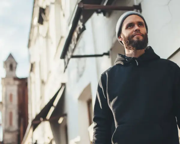 Mężczyzna w czarnej bluzie z kapturem i czapce beanie patrzy w górę. Stylowy sposób, jak nosić bluzę z kapturem.