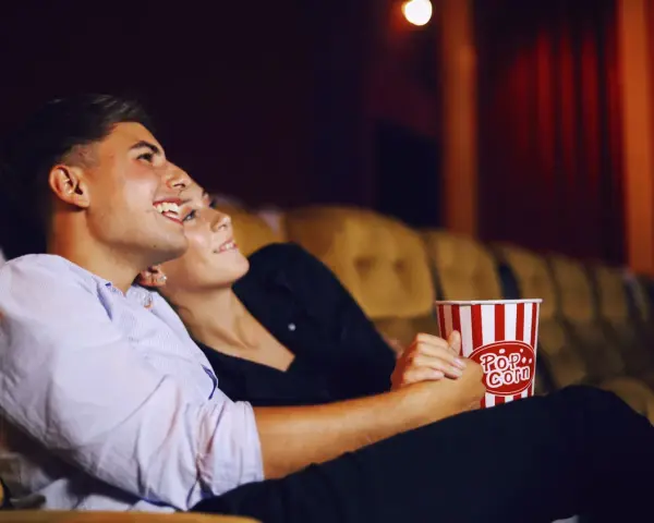 Para randkę do kina wybierz wygodny, ale stylowy strój. Para siedzi blisko siebie, trzymając popcorn.