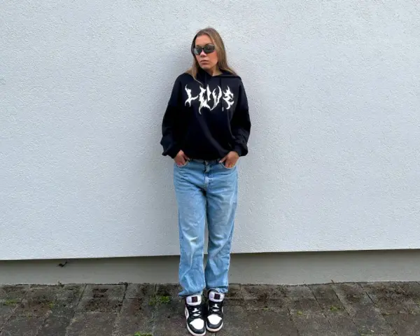 Dziewczyna w czarnej bluzie z kapturem i jeansach, idealny outfit, jak się ubrać na koncert hip hopowy.