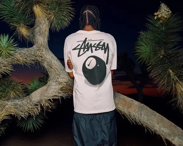 Mężczyzna w koszulce Stussy z grafiką kuli bilardowej 8 i logo Nike. Stussy to kultowa marka streetwearowa.