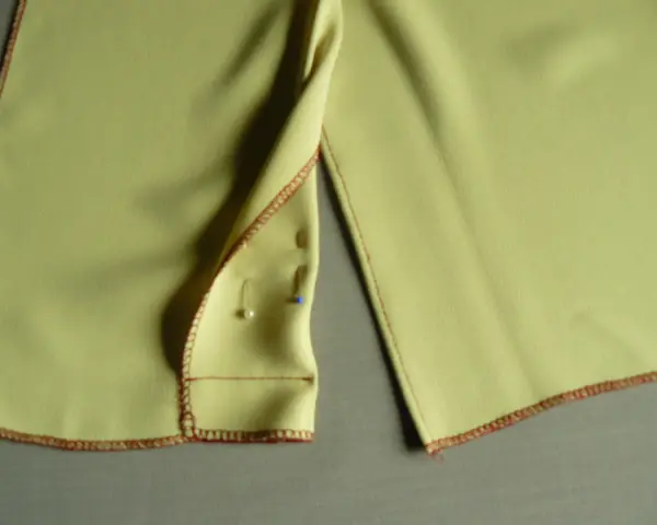 Szczegółowy widok na żółtą sukienkę, pokazujący, jak zrobić rozporek. Widoczne szpilki i czerwone obszycie.