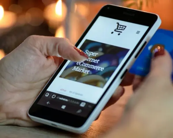 Kobieta z kartą kredytową w dłoni przegląda na smartfonie stronę e-commerce, ucząc się, jak sprzedawać bieliznę w internecie.