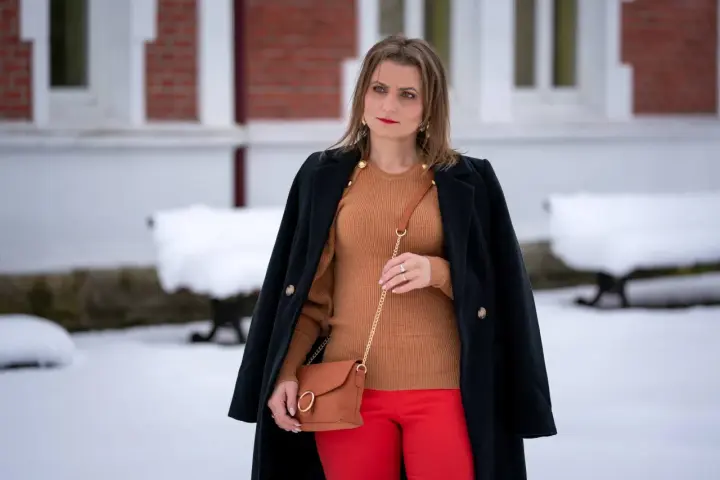 Elegancka stylizacja: co ubrać do czerwonej spódnicy? Brązowy sweter, czarny płaszcz i karmelowa torebka tworzą stylowy zestaw.