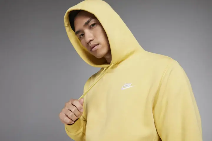 Młody mężczyzna w żółtej bluzie z kapturem Nike Club.