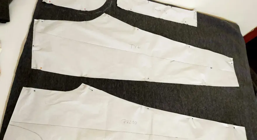 Wykroje papierowe do spodni (przód i tył) przypięte do ciemnego materiału. Rozpoczynamy proces, jak zrobić wykrój spodni.