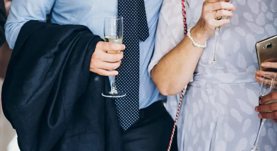 Elegancki mężczyzna w garniturze i krawacie, trzymający kieliszek szampana. To idealny strój, co się ubiera na bierzmowanie.