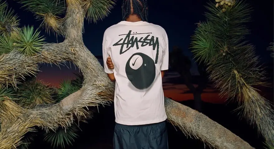 Mężczyzna w koszulce Stussy z grafiką kuli bilardowej 8 i logo Nike. Stussy to kultowa marka streetwearowa.
