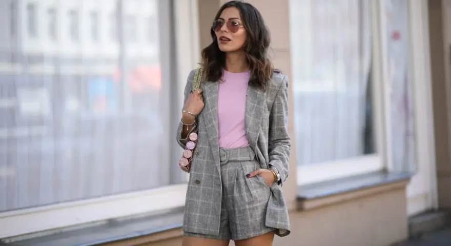 Elegancka stylizacja: co ubrac do spódnico spodenek? Szary garnitur w kratę, różowy top i modna torebka.